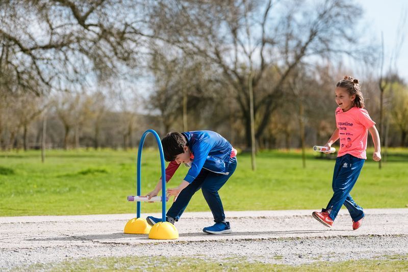 Dos niños juegan al aire libre con un arco azul en un sendero. Uno se inclina, el otro corre hacia adelante
